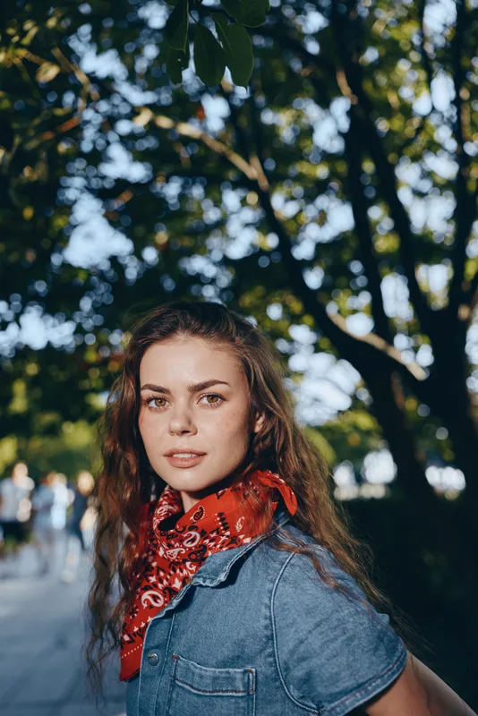 lifestyle woman in modern boho-western denim street style poses outdoors with soft film color tones enhancing natural light and casual urban vibe in summer setting