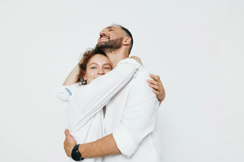 A professional man expresses triumph while embracing a colleague against an isolated colored background, conveying confidence, warmth, and positive business emotion.