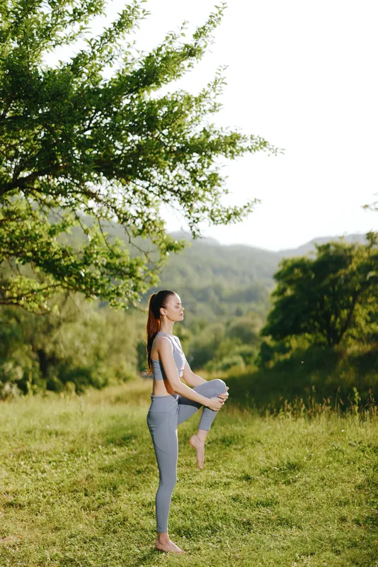 Young woman practicing yoga in a serene outdoor setting, wearing comfortable athletic wear, showcasing balance and focus in a lush green landscape