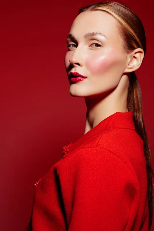 Portrait of a confident woman with sleek hair and red lipstick wearing a red outfit against a red background. Concept of fashion, beauty, and elegance in studio lighting.