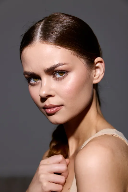 beauty woman with smooth skin, braided hair, and natural makeup posing against dark background, showcasing flawless complexion and subtle glow