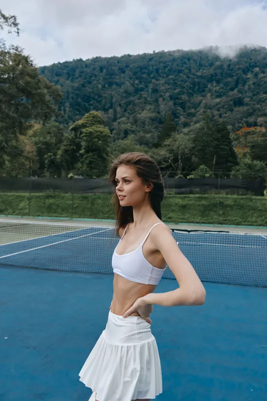Young athletic woman enjoying tennis outdoors with a scenic background, dressed in a stylish white sports outfit, exuding confidence and joy