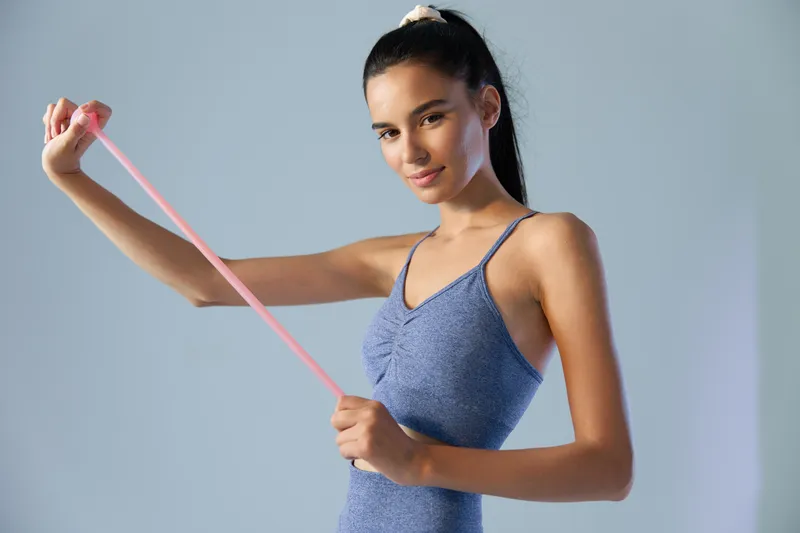 woman sport fitness stretching with resistance band in blue activewear, smiling young woman exercising, indoor light background, healthy lifestyle concept