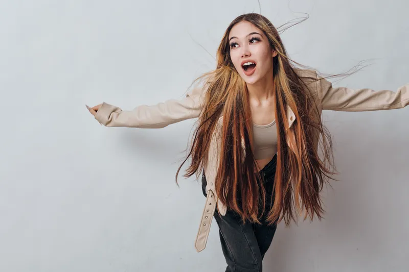 Woman with long braids posing with arms outstretched and surprised expression on white background for fashion and hairstyle concept.