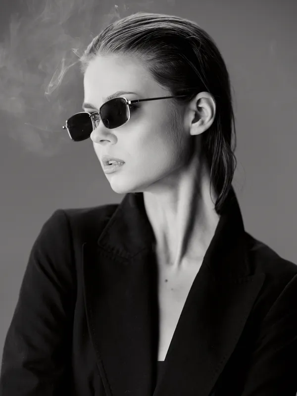 Black and white portrait of a stylish woman wearing sunglasses and a blazer with a confident expression