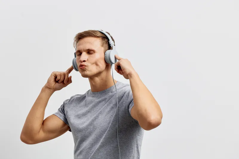 Smiling man wearing gray t-shirt listening to music with headphones, cheerful expression, casual style, light background, studio shot, leisure activity, lifestyle concept.