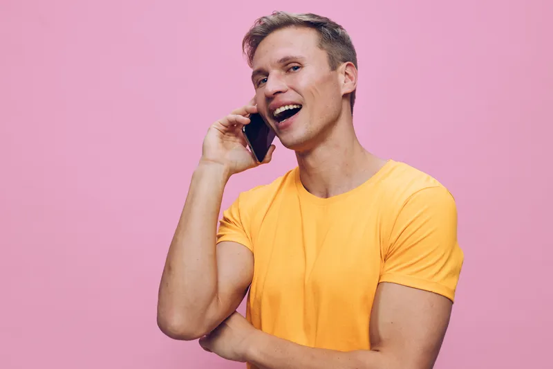 smiling man talking phone wearing yellow t-shirt isolated pink background cheerful young person digital nomad communication concept