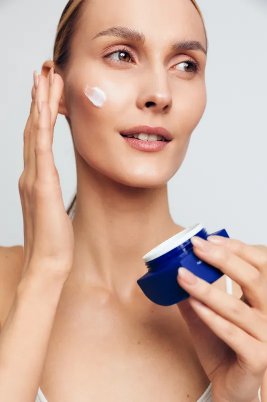 Closeup of a woman applying moisturizer to her face, soft studio lighting, clear skincare concept, natural glow, calm expression, clean background, beauty routine moment, healthy skin