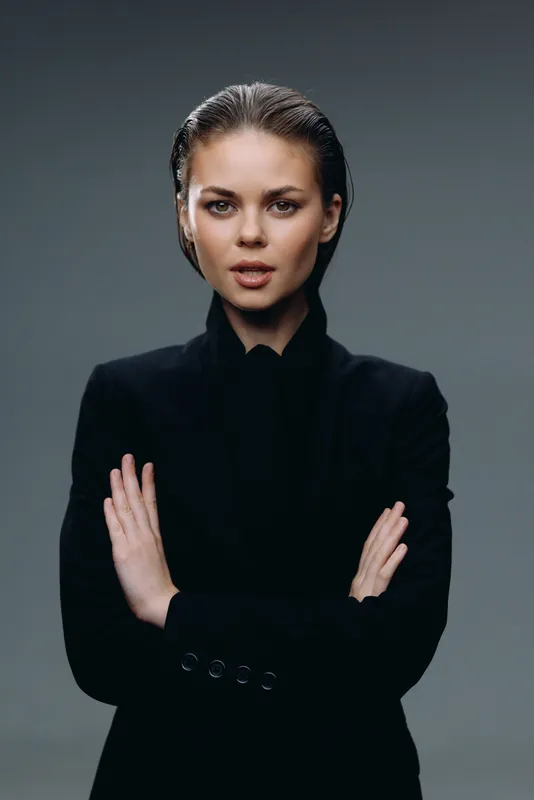 Confident woman with crossed arms in black outfit against dark background, showcasing strength and determination.