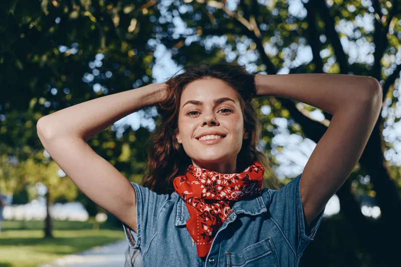 Lifestyle woman in modern boho-western denim street style smiling outdoors with a red bandana, film color, natural lighting, and casual confident pose.
