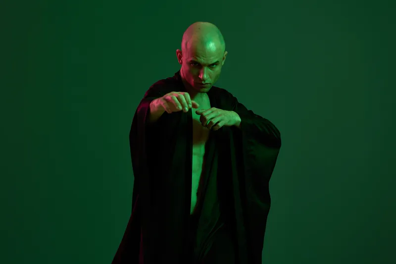 Intense man in a striking pose, showcasing martial arts skills with a dramatic black outfit against a vivid green backdrop. A bold and energetic black and white composition.