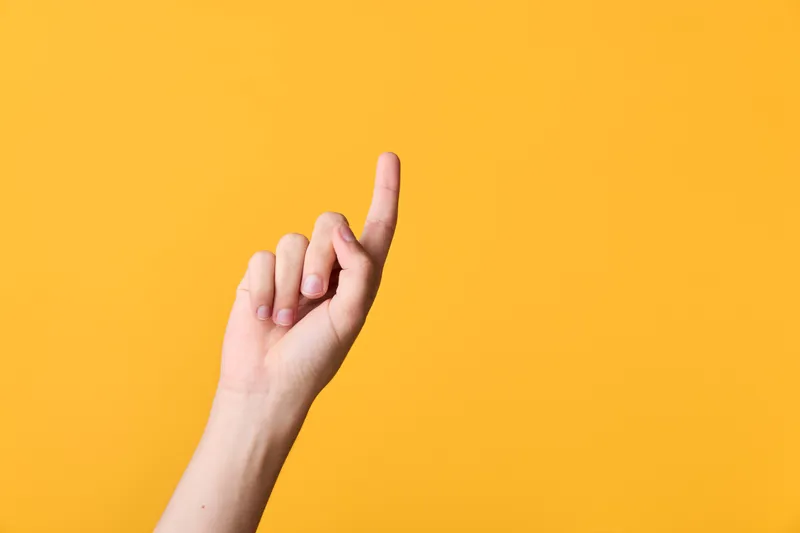 Close up of a hand with the index finger raised, gesturing upward against a bright orange backdrop, emphasizing focus, direction, and a minimal, modern visual cue suitable for banners and tutorials