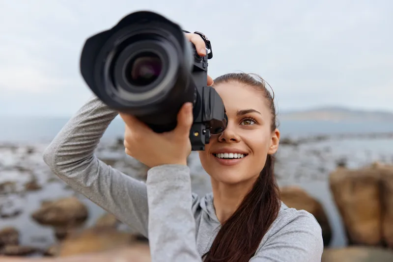 Young woman with a camera on the beach, capturing stunning photography, showcasing joy and creativity in a serene coastal environment
