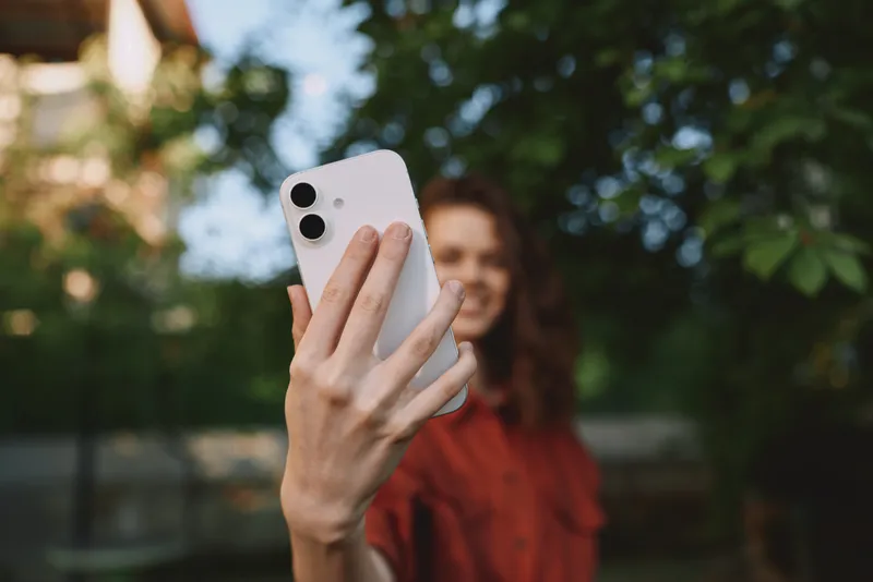 Woman taking a selfie with a smartphone outdoors, showing a cheerful lifestyle and portrait mood, with sunlight and greenery creating a warm natural atmosphere for everyday self care