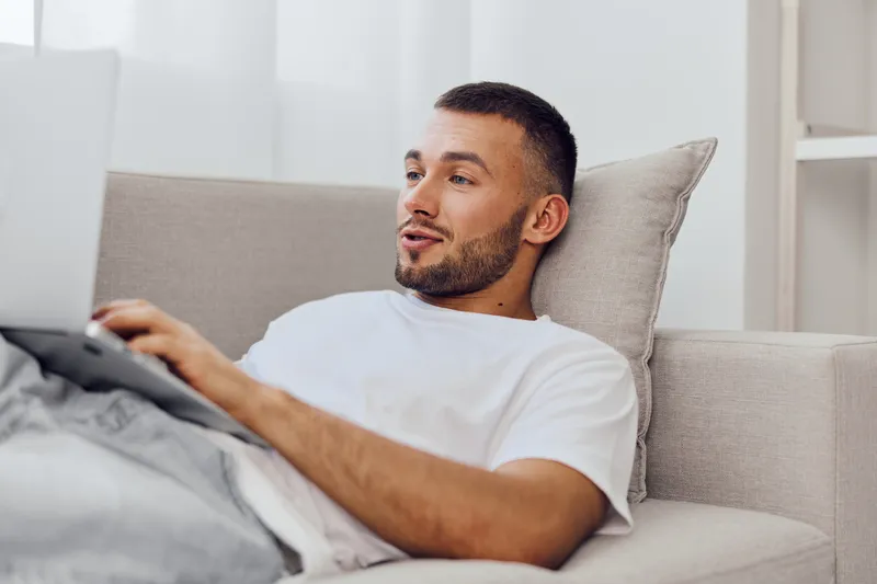 Smiling man working at home on laptop, dressed casually, with a relaxed expression and cozy atmosphere, showcasing modern lifestyle and productivity.