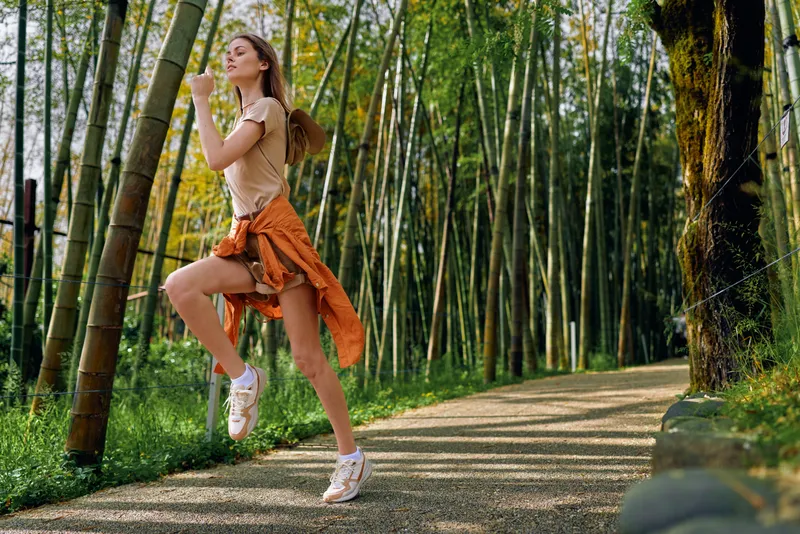 Woman running exercise park bamboo trail fitness outdoor runner leaping with ponytail, athletic outfit and sneakers, healthy lifestyle and jogging on a green forest path.