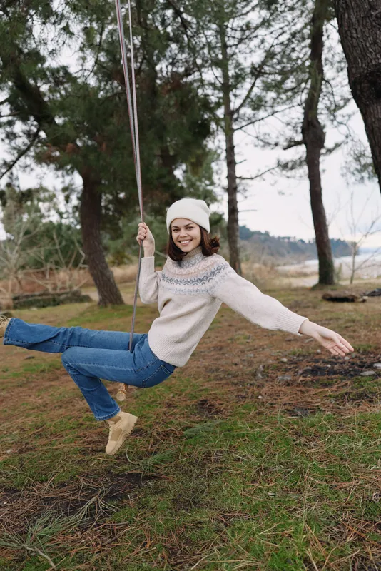 Woman on a swing in a park, outdoors on a crisp winter day, wearing a cozy sweater and boots. Playful, candid moment with natural movement in a peaceful outdoor setting.