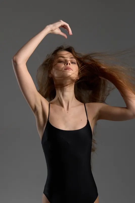 graceful woman dancing with flowing hair in black bodysuit against gray background