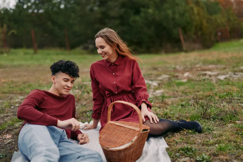 A candid outdoor moment shows a pair sharing a simple picnic on a blanket, capturing authentic, credible emotion and a genuine, relaxed connection between friends under warm light.