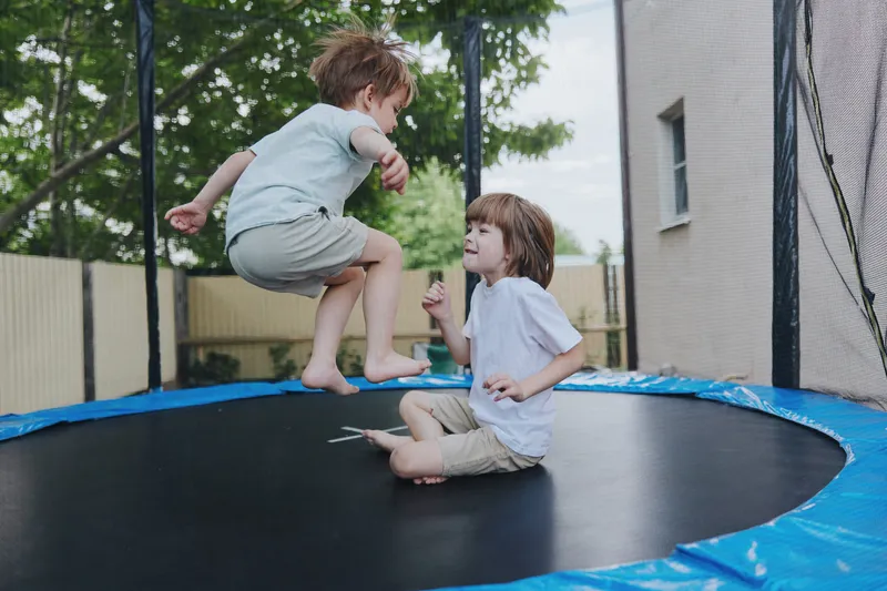 Happy children playing on a trampoline, enjoying a sunny day outdoors, filled with laughter and joy in a vibrant backyard setting.