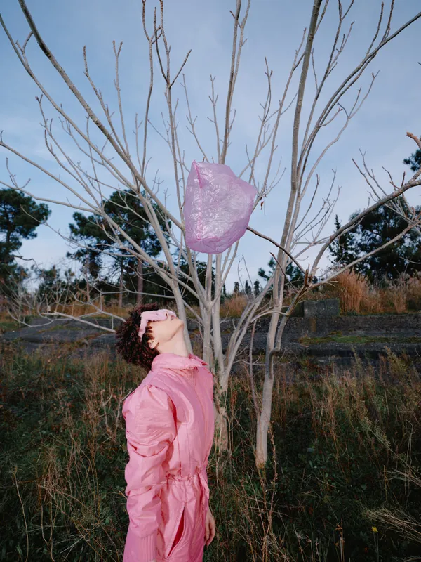 Woman in pink dress releasing a pink balloon in an open field with bare trees, capturing a moment of imagination, freedom and outdoor creative expression.