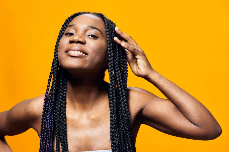 Joyful young woman with braided hair against a vibrant yellow background, showcasing confidence and happiness, ideal for beauty and self care concepts