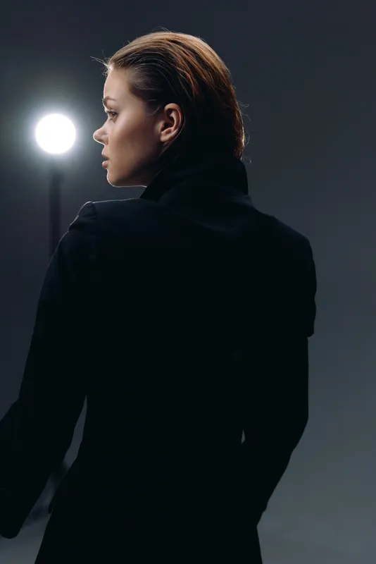 Profile of a thoughtful woman in black coat with short hair against dark background.