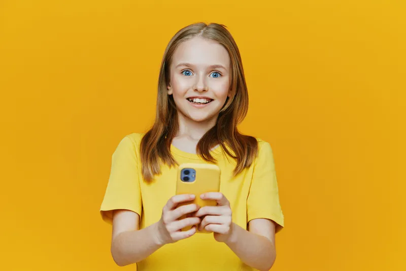 Happy girl with smartphone on yellow background, showcasing joy and excitement, wearing a bright yellow shirt, perfect for children s lifestyle and technology themes