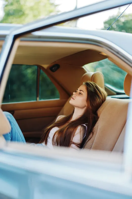 Young woman relaxing in a car with long hair against a natural background, embodying comfort, tranquility, and a carefree lifestyle during summer days.