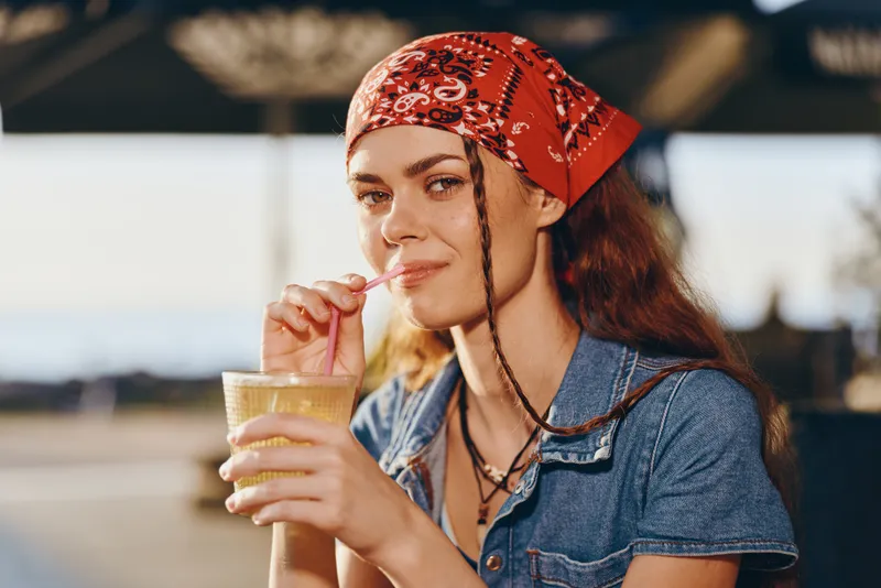 lifestyle woman in modern boho-western denim street style with red bandana enjoying drink, film color tone enhancing warm natural light and casual summer vibe