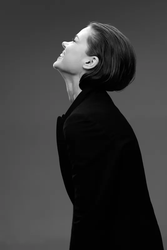 Smiling woman in black coat looking up in black and white portrait with dark background
