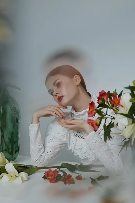 Serene young woman in a white lace blouse, surrounded by vibrant flowers, creating a fresh and natural atmosphere showcasing beauty and elegance