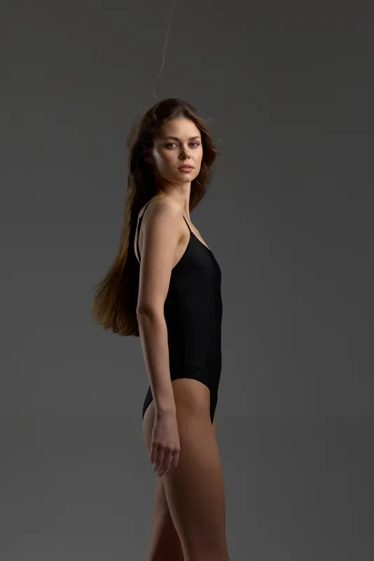 Young woman in black bodysuit posing confidently with natural expression on dark gray background