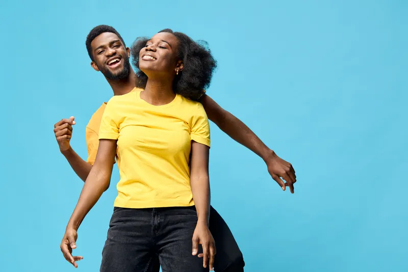 Joyful couple having fun together against a bright blue background, wearing matching yellow t shirts, expressing happiness and connection