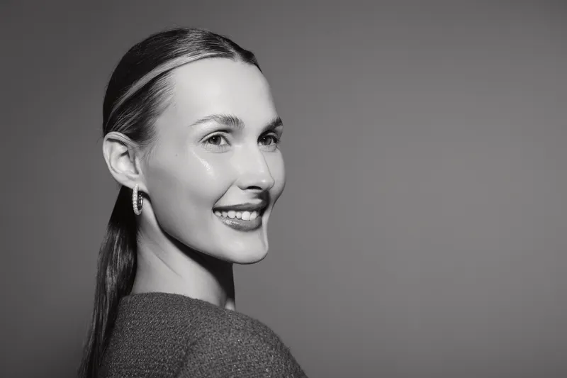 Smiling Caucasian woman with fair skin and long hair looks over shoulder in grayscale portrait. Natural beauty concept with positive facial expression and soft lighting.