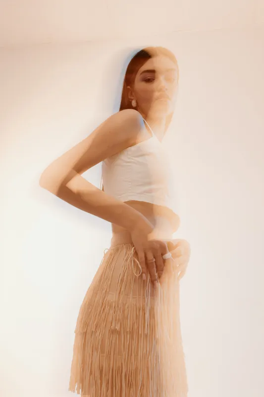 Blurred motion portrait of a woman in a white top and beige skirt. The artistic effect highlights beauty and fashion with soft lighting on a light background.