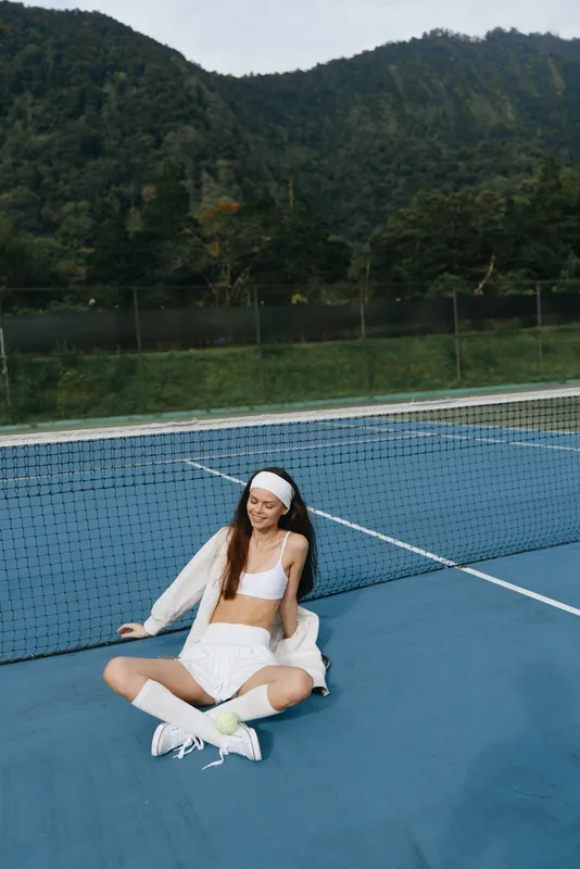 Young Asian woman enjoying a playful moment on a tennis court, wearing sporty attire and exuding joy amidst a lush green background