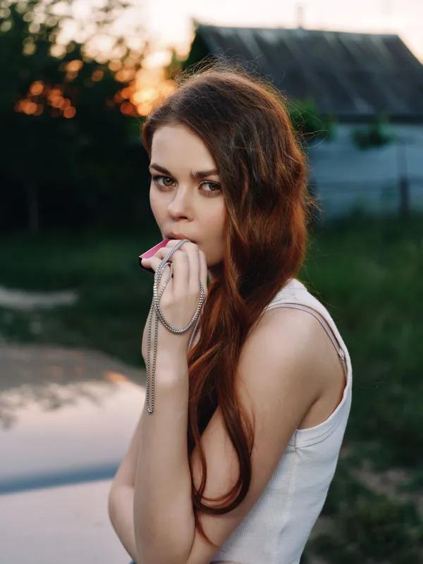 Young woman with long red hair holding a whistle, evoking determination in a natural outdoor setting during sunset.