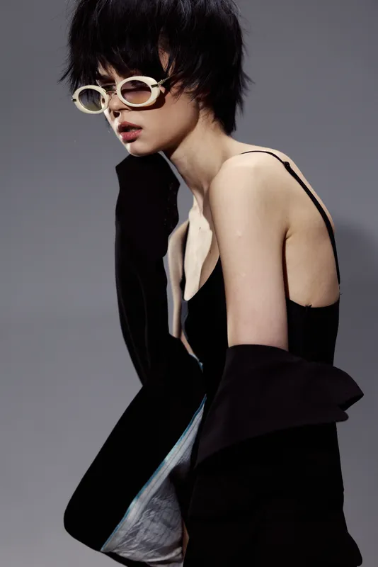 Stylish woman wearing oversized sunglasses and black jacket with bare shoulder in modern fashion look