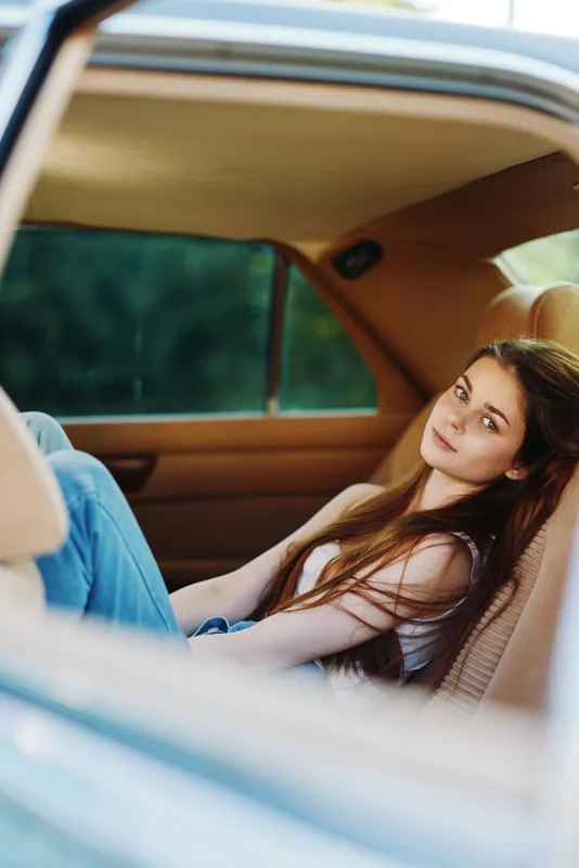 Young woman relaxing in car, wearing casual outfit, enjoying serene moment, with warm tones and green background, captures tranquility and youthfulness.