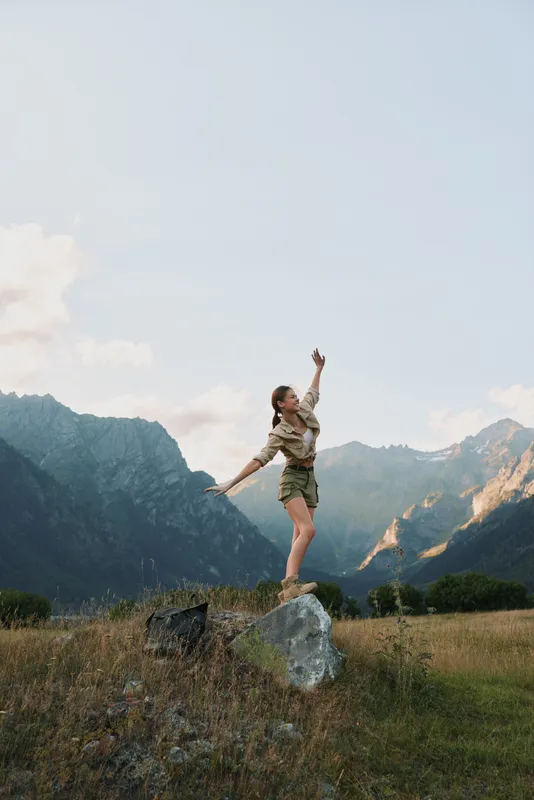 Young woman balances on a rock in a mountain meadow, enjoying fresh air and freedom.