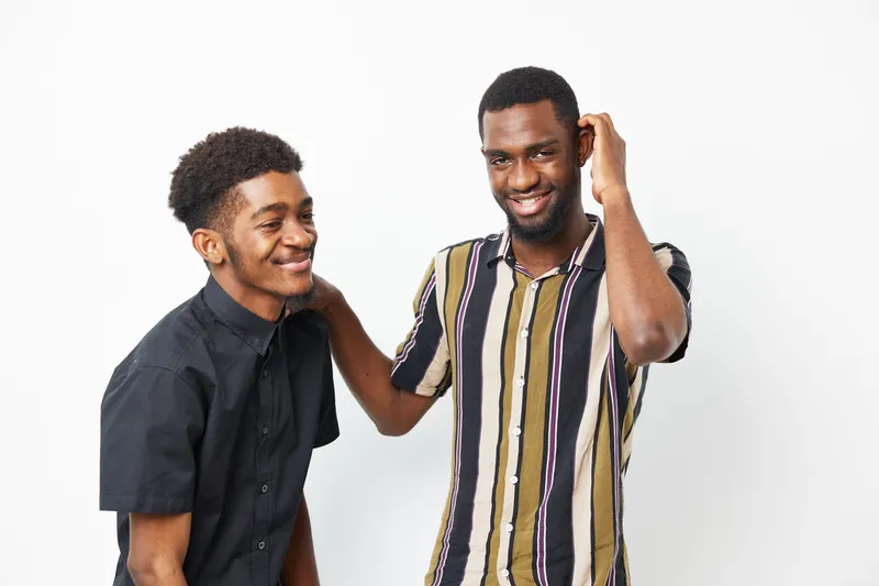 Two smiling African American men enjoy a light-hearted moment together, showcasing camaraderie and joy against a clean, minimalist background.