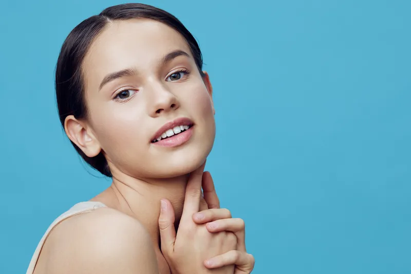 Young woman with fresh skin and gentle expression against a blue background, showcasing beauty and self care, ideal for health and wellness concepts