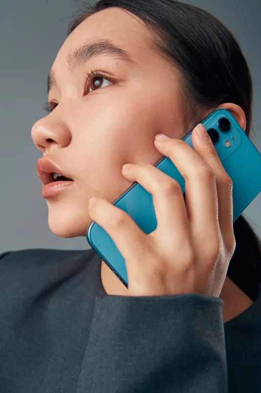 Young woman holding blue smartphone to ear for communication and conversation with focused expression. Technology, mobile phone, connection, and digital communication closeup.