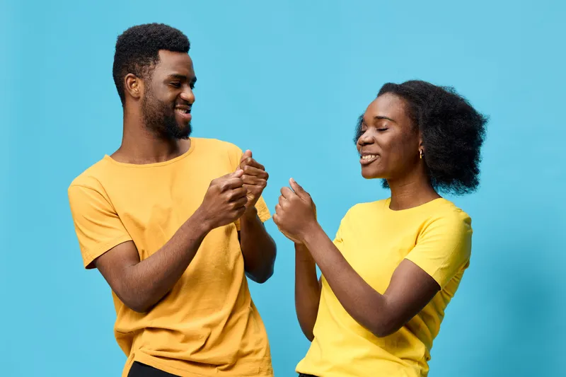 Happy young African couple dancing and enjoying time together on a vibrant blue background, wearing matching yellow t shirts that reflect joy and positivity
