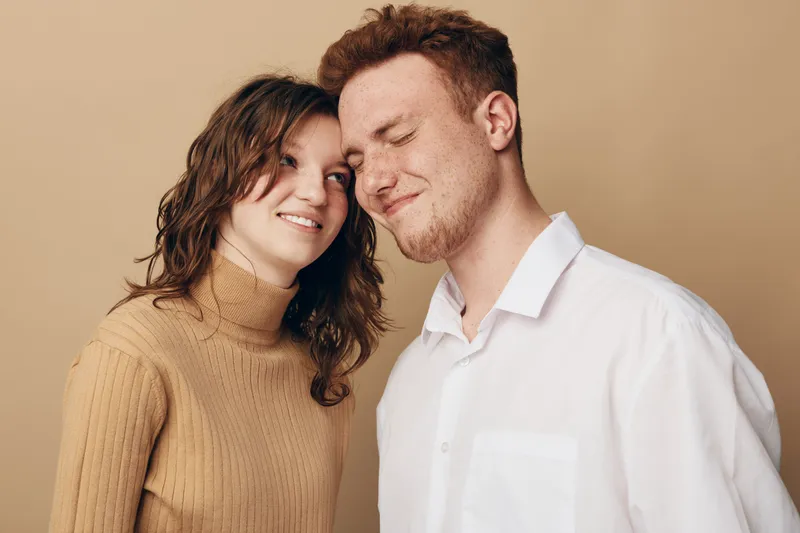 Young couple in casual clothing shares a tender moment, smiling and close together against a neutral background. Concept of love, affection, and relationship intimacy.