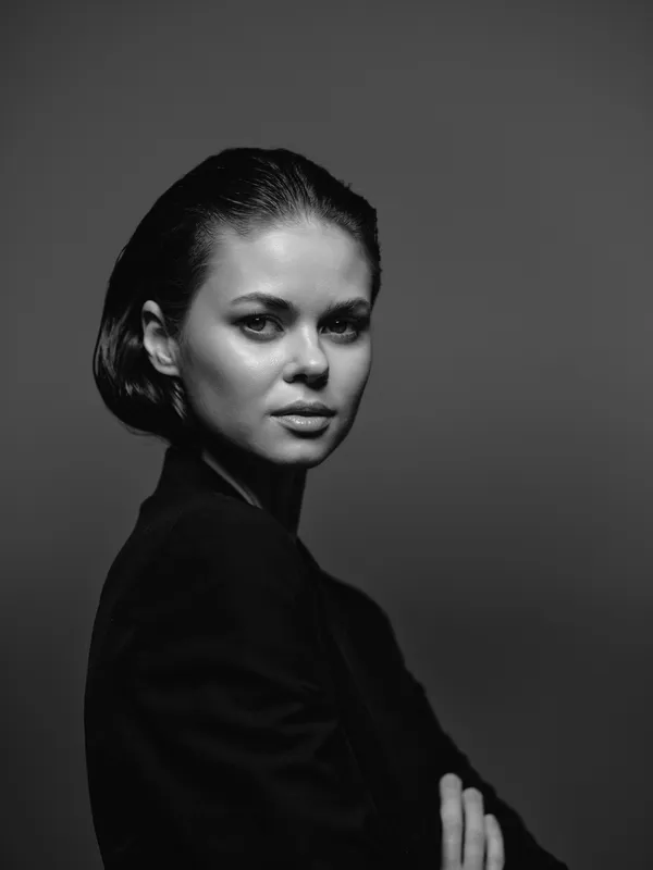 Black and white portrait of a serious woman with short hair in a dark outfit against a studio background.