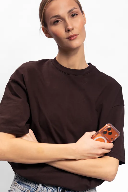 Young woman in brown shirt holding smartphone with crossed arms looks confidently at camera on white background. Concept of technology, casual style, and modern lifestyle portrait.