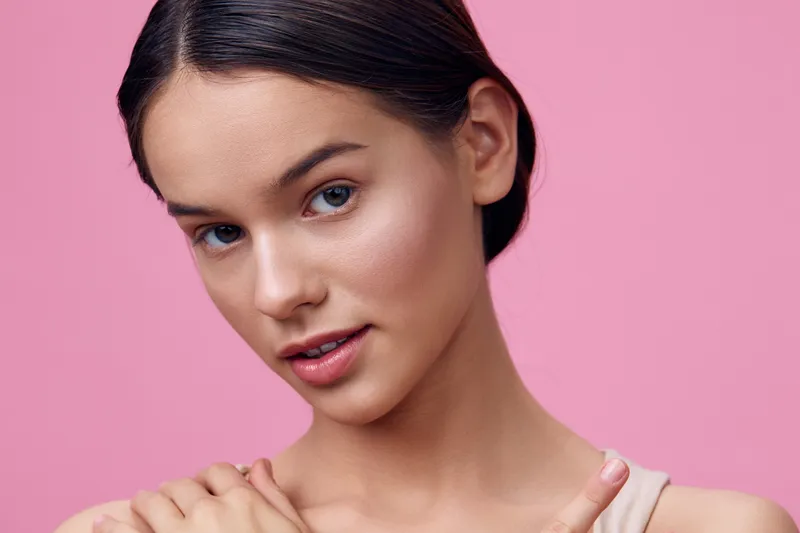 Portrait of a young model with a natural look and soft expression against a pink background, emphasizing beauty, femininity, and self confidence