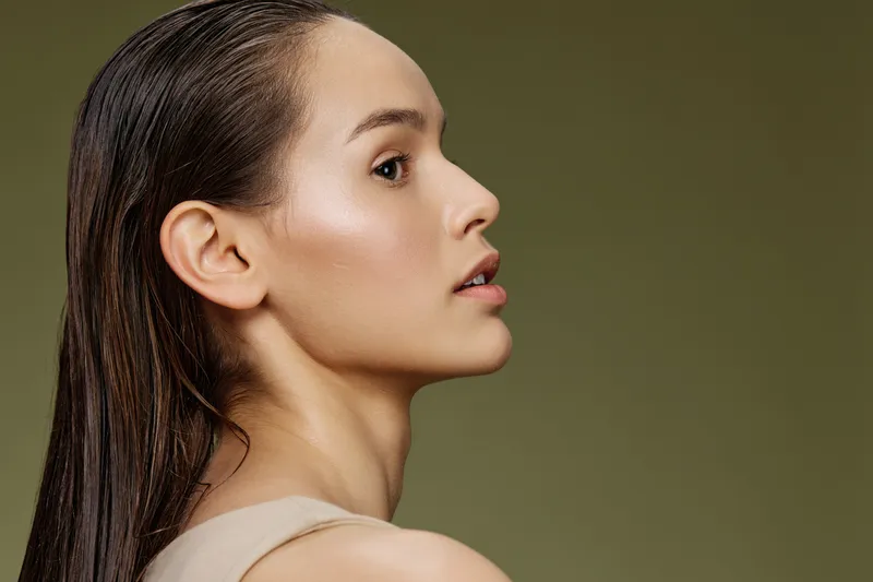 Elegant portrait of a young woman with long, wet hair on a soft green background, showcasing natural beauty and delicate features